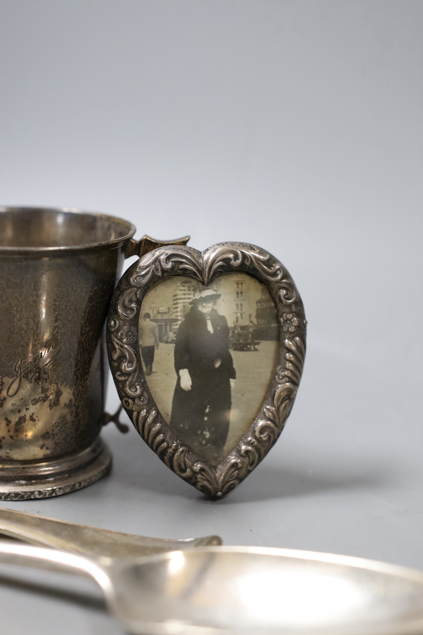 Two 18th century silver spoons, a later silver christening mug, small silver mounted heart shaped photograph frame, a silver napkin ring and a silver handled button hook.